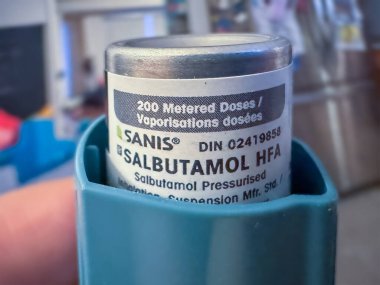 Calgary, Alberta, Kanada. 29 Nisan 2025. Sanis Salbutamol HFA inhaler tüpünün yakın plan görüntüsü. Etikette dozaj bilgisi ve DIN numarası var. Kısmen bir deniz mavisi çalıştırıcısına yerleştirilmiş..