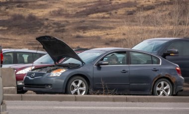 Calgary, Alberta, Kanada. 24 Nisan 2025. Gri bir Nissan Altima kaputu açık ve patlak bir lastikle park halinde. Arabanın içinde bir kişi görünüyor. Araç yol kenarında gibi görünüyor..