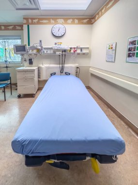 Calgary, Alberta, Kanada. 25 Nisan 2025. Hasta yatağı, tıbbi ekipman, saat ve hayvan temalı süsleme içeren temiz ve düzenli bir hastane muayene odası..