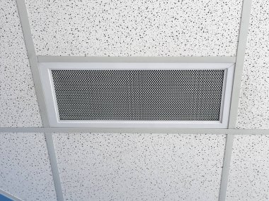 Dikdörtgen şeklinde, delinmiş metal ızgara, bir Ventlab, benekli desenli asılmış bir tavana monte edilmiş. Izgaranın gümüş bir çerçevesi var ve tavan kiremitleri ve destek yapısı içinde ortalanmış..