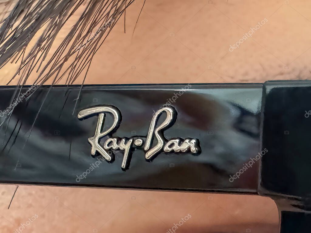 Calgary, Alberta, Canada. Apr 29, 2025. Close-up of the Ray-Ban logo in silver lettering on a glossy black frame, possibly sunglasses, with a blurred background and hair visible at the top.