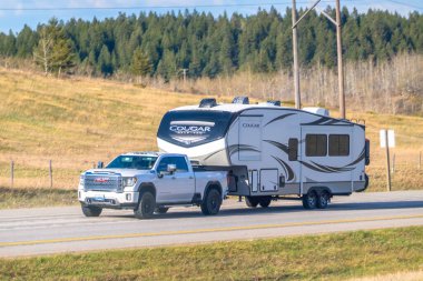 Canmore, Alberta, Kanada. 5 Mayıs 2025. Beyaz bir GMC Sierra kamyonet 2021 Keystone Cougar 290RLS beşinci tekerlek römorkunu kırsal alanda bir otoyolda çekiyor..