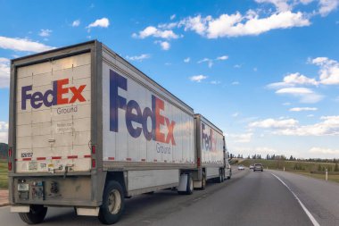 Canmore, Alberta, Kanada. 5 Mayıs 2025. Beyaz bir FedEx Ground çift karavan kamyonu parçalı bulutlu bir gökyüzünün altında bir otoyolda gidiyor. Diğer araçlar uzaklıktan görülebilir..