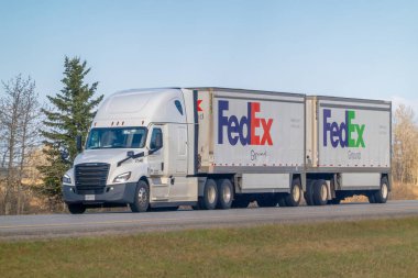 Rocky View County, Alberta, Kanada. 5 Mayıs 2025. Bir FedEx Ground çift karavan kamyonu açık bir gökyüzü altında karayolu boyunca seyahat ederek, lojistik ve arazide mal dolaşımını sembolize ediyor..