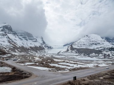 Jasper, Alberta, Kanada. 4 Mayıs 2025. Kolombiya 'nın buzul bölgesinde kısmen kar ve buzla kaplı engin, dağlık bir arazi. Yollar bulutlu bir gökyüzünün altında ön planda esiyor..