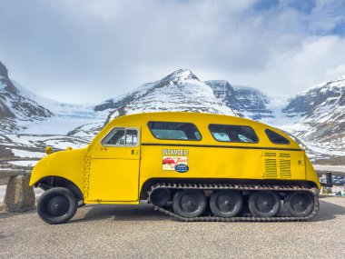 Jasper, Alberta, Kanada. 4 Mayıs 2025. Sarı kar motosikletli bir tur aracı. Arkasında kar örtülü dağların izleri var..