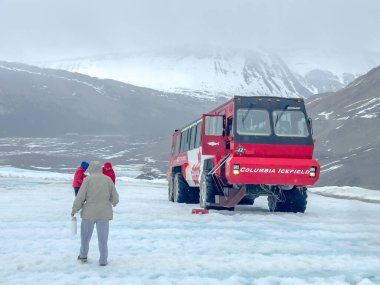Jasper, Alberta, Kanada. 4 Mayıs 2025. Kırmızı bir Columbia Buzul Macerası otobüsü. Arkasında karlı dağlar var. Otobüsün yanında insanlar görünüyor..