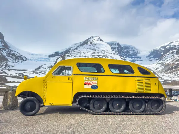 Jasper, Alberta, Kanada. 4 Mayıs 2025. Sarı kar motosikletli bir tur aracı. Arkasında kar örtülü dağların izleri var..
