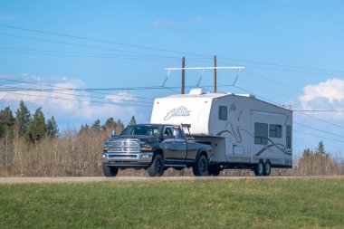 Calgary, Alberta, Kanada. 9 Mayıs 2025. Siyah bir Dodge RAM 2500 çekici beyaz 2001 Lakota 5. Tekerlek römorku üzerinde elektrik kabloları ve çimenli bir tarla ile yol boyunca çekilir..