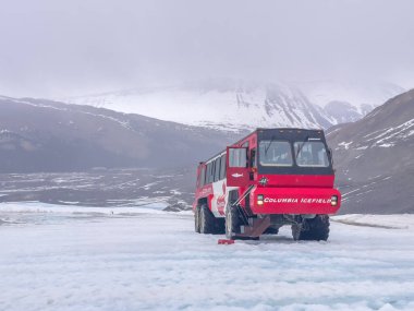 Jasper, Alberta, Kanada. 9 Mayıs 2025. Bir kırmızı buz kaşifi otobüsü, Kolombiya Buzul Macerası 'nın bir parçası olan karlı bir arazide görkemli ve sisli dağlara karşı yol alır..