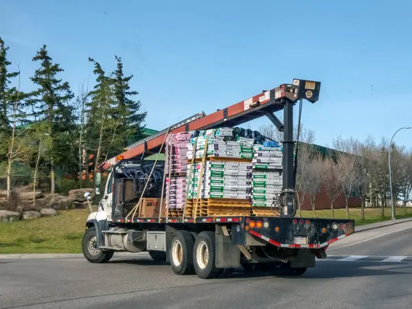 Calgary, Alberta, Kanada. 9 Mayıs 2025. Bir vinç nakliye kamyonu ile donatılmış çatı kiremitleri, Elit Çatı Teçhizatı, açık bir gökyüzünün altındaki yol boyunca.
