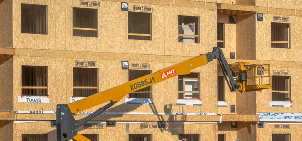 Calgary, Alberta, Kanada. 9 Mayıs 2025. Sarı eklemli bir patlama asansörü kısmen inşa edilmiş bir binaya doğru uzanır. Platformu ahşap çerçeveli yapının üst katlarına ulaşır..