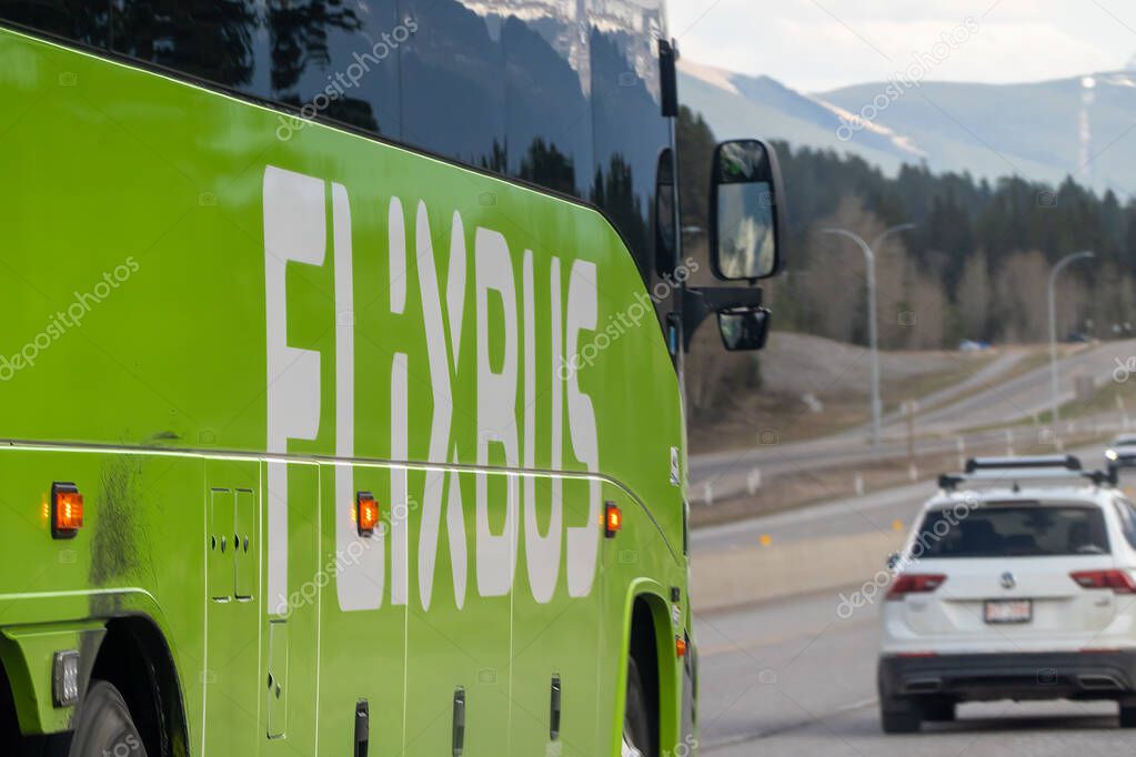 Canmore, Alberta, Canada. May 9, 2025. A green Flixbus travels on a highway, with mountains visible in the background.