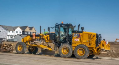 Calgary, Alberta, Kanada. 15 Mayıs 2025. Gökyüzünün altındaki bir inşaat alanının ön planında büyüyen şehrin altyapı gelişimini işaret eden sarı bir tırtıl motoru..