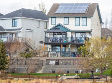 Calgary, Alberta, Kanada. 16 Mayıs 2025. Güneş panelleri ve yeşil alana uzanan katlı bir arka bahçeyle güçlendirilmiş, iki katlı evlerin olduğu bir bodrum katı. Kenar mahallelerde yaşamak sürdürülebilirlikle karşılaşıyor.