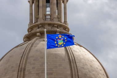Edmonton, Alberta, Kanada. 21 Mayıs 2025. Alberta Yasama Binası 'nın görkemli kubbesi, eyalet bayrağının yer aldığı, bulutlu gökyüzüne gururla karşı duruyor, yönetim ve mirası simgeliyor..