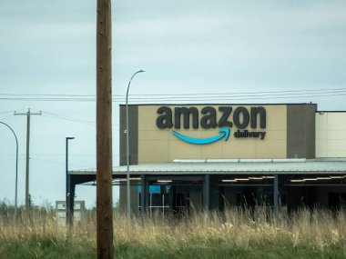 Edmonton, Alberta, Kanada. 24 Mayıs 2025. Amazon Teslimat binası bulutlu bir gökyüzünün altında duruyor, kendine özgü logosu hızlı bir e-ticaret vaadediyor, küresel lojistiğin anahtar merkezi..
