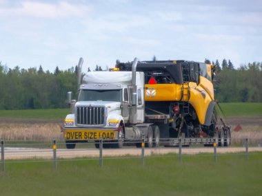 Edmonton, Alberta, Kanada. 24 Mayıs 2025. Ağır bir nakliye kamyonu, tarım makineleri için gerekli lojistiği gösteren büyük ölçekli bir hasat aracını taşıyor..
