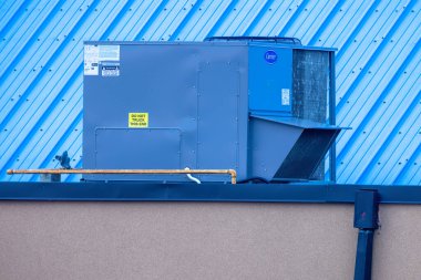 Edmonton, Alberta, Kanada. 27 Mayıs 2025. Bir çatı taşıyıcı HVAC ünitesi, ticari ve endüstriyel ortamlar için gerekli iklim kontrolünü sembolize eden mavi kıvrımlı bir duvara karşı belirgin bir şekilde duruyor..