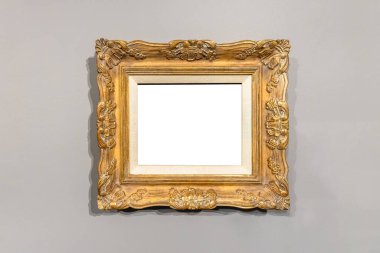 Süslü detaylarıyla antik bir altın çerçeve ve nötr bir duvara asılı beyaz bir halı, el değmemiş sanat eserlerini sergilemek için klasik bir estetik sunuyor..