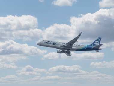 Calgary, Alberta, Kanada. 27 Mayıs 2025. Bir Alaska Havayolları Embraer 175, bulutlu gökyüzünde zarif bir şekilde süzülür, modern bölgesel hava yolculuğunun sembolü ve verimli bir bağlantı..
