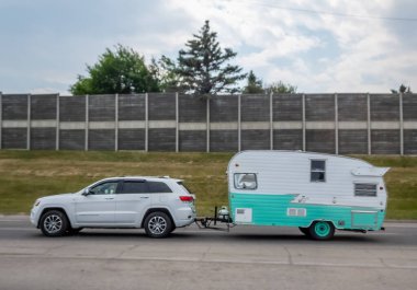 Calgary, Alberta, Kanada. 8 Haziran 2025. Beyaz bir SUV, geçmişe dönük, deniz mavisi ve beyaz bir Shasta Airflyte seyahat karavanını çekiyor. Nostaljik macera ve modern bir yolculuk hissi uyandırıyor..