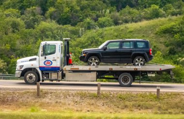 Calgary, Alberta, Kanada. 8 Haziran 2025. Bir CAA çekicisi yolda siyah bir SUV taşıyor. Çerçevesi yemyeşil tepelerle çevrili. Güvenilir yol yardımını simgeliyor..