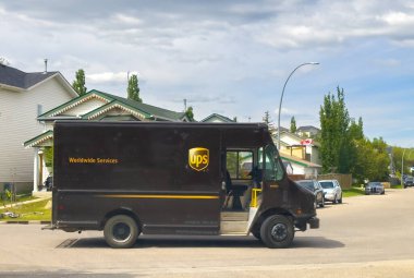 Calgary, Alberta, Kanada. 8 Haziran 2025. Tanıdık bir UPS kamyonu, dijital çağda toplumları birbirine bağlayan temel dağıtım hizmetlerini sembolize ederek, ağaçlarla kaplı bir yerleşim bölgesinde geziniyor.