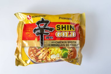 Calgary, Alberta, Kanada. 14 Haziran 2025. Bir paket Nongshim Shin Gold tavuk suyuyla hazır şehriye, parlak bir altın tasarımı, temiz beyaz bir arkaplana karşı..