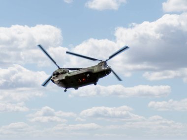 Calgary, Alberta, Kanada. 14 Haziran 2025. Güçlü bir Boeing CH-47 Chinook askeri helikopteri bulutlu bir gökyüzünde süzülüyor ve uçuşta kendine özgü ikili rotor tasarımını gösteriyor..