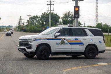 Calgary, Alberta, Kanada. 25 Haziran 2025. Koyu mavi ve sarı çizgili el değmemiş bir RCMP polis cipi bulutlu gökyüzü altında devriye geziyor, kanun ve düzeni somutlaştırıyor..