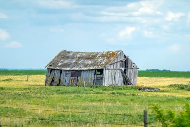 Harap olmuş ahşap bir kulübe, bulutlu bir gökyüzünün altında ıssız, yeşil bir çayır tarlasında duruyor. Bu da Kanada Alberta 'da terk edilme ve kırsal tarihi çağrıştırıyor..