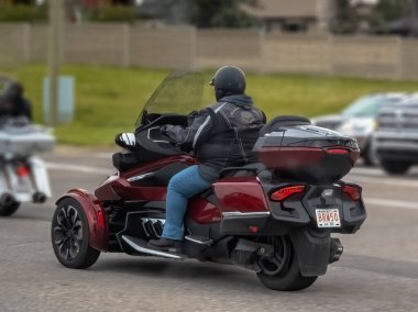 Calgary, Alberta, Kanada. 18 Haziran 2025. Gösterişli, koyu kırmızı bir Konserve-Am Spyder motosikleti yolda, benzersiz üç tekerli tasarımı ve tam teçhizatlı bir sürücüsü var, özgürlüğü ve açık yol reklamını vurguluyor.