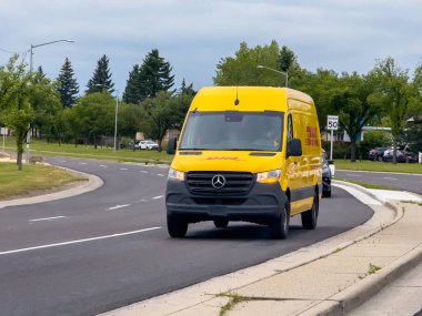 Calgary, Alberta, Kanada. 26 Haziran 2025. Canlı bir DHL dağıtım aracı Calgary 'de virajlı bir yolda ilerliyor, etkin lojistik ve paket teslimat hizmetlerini kentsel bir ortamda gösteriyor..