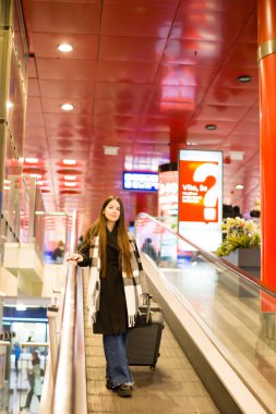 Bavuluyla yürüyen merdivenden inen şık bir kadın, seyahat ve hareket teması için mükemmel. Yüksek kalite fotoğraf