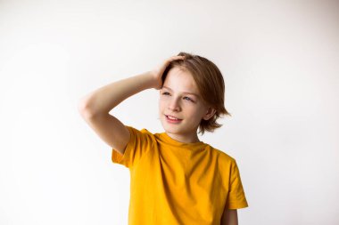 Genç bir çocuk, düz beyaz bir arka plan karşısında duran düşünceli bir ifadeyle mesafeye bakar. Yüksek kaliteli fotoğraf..