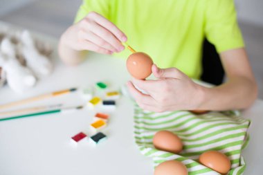 Boya fırçasını tutan, Paskalya yumurtasını süsleyen küçük ellerin yakın çekimi. Tatil, yaratıcılık ve Paskalya kutlaması kavramı. Yüksek kaliteli fotoğraf..