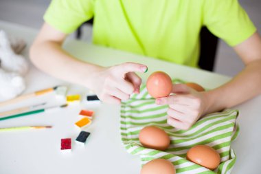 Genç bir çocuk, parmaklarını neşeli bir şekilde Paskalya yumurtasını renkli boyayla süslemek için kullanıyor. Paskalya kutlaması, yaratıcı el sanatları ve tatil eğlencesi kavramı. Yüksek kaliteli fotoğraf..