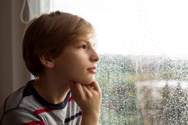 Yağmurla kaplı bir pencereden bakan dalgın bir çocuk. Düşünce, sakinlik, çocukluk düşünceleri. Yüksek kaliteli fotoğraf..