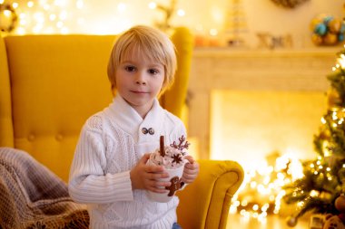 Tatlı çocuk, oğlum, Noel için süslü bir odada sarı bir koltukta oturuyor, rahat bir yer.