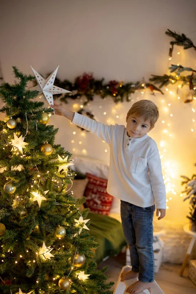かわいい就学前の子供 ブロンドの男の子はクリスマスツリーを飾る トップに星を置く 自宅でクリスマスルームを飾る — ストック写真