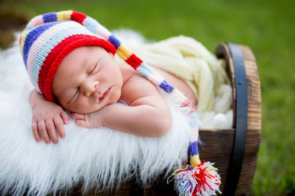 公園で屋外ガーデンでニットのカラフルな帽子のクレートに寝て甘い新生児男の子 — ストック写真