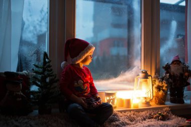 Güzel çocuk, evlat, Noel arifesinde pencerenin önünde Noel Baba 'yı merakla bekliyor.