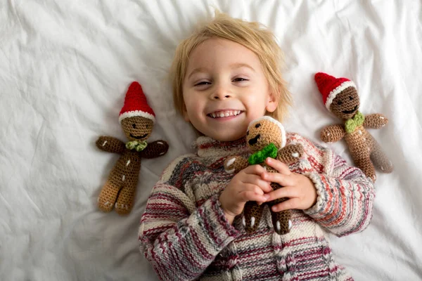 Cute toddler child, holding knitted toy, sitting in bed, playing with pet dog, wearing santa hat