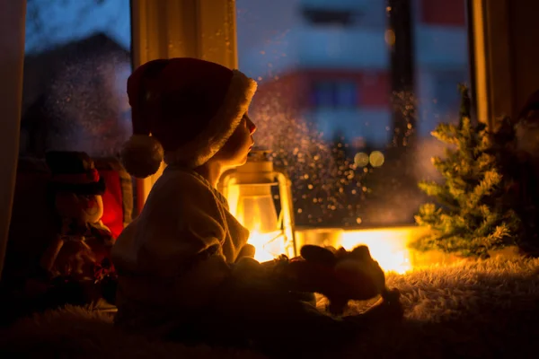 かわいい子供は 窓の上に座って サンタクロースを探して屋外で 窓のクリスマスの装飾 — ストック写真