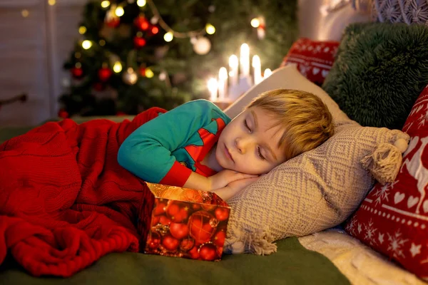 Cute preschool child, blond boy with pet dog, opening presents at home, decorated Christmas room  at home