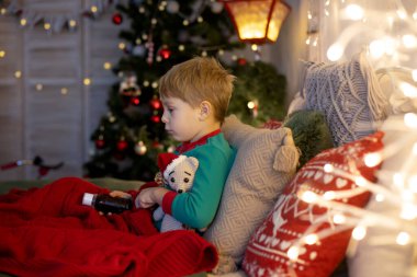 Küçük sarışın çocuk, yatağında hasta yatıyor, şurup içiyor, üzülüyor.