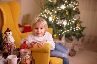 Sevimli çocuk, oğlum, Noel 'de anne ve büyükanneyle süslü bir odada sarı koltukta oturuyor.