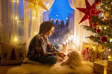 Küçük bir çocuk, tatlı sarışın çocuk, pijamayla pencerede oturuyor, Satna Claus 'a bakıyor, kurabiye yiyor, Noel ışıklarını yakıyor.