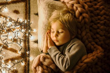 Küçük çocuk, tatlı sarışın çocuk, geceleri yatağında Noel ışıklarıyla uyuyor.